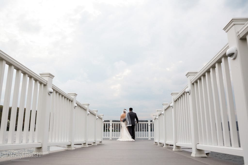 A bride and a groom standing at the end of a white dock overlooking Candlewood Lake